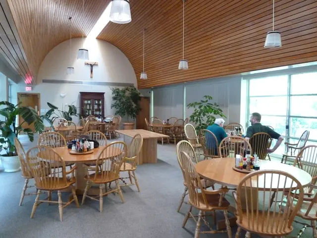 This picture shows few chairs and tables and we see plants and couple of them seated on the chairs...